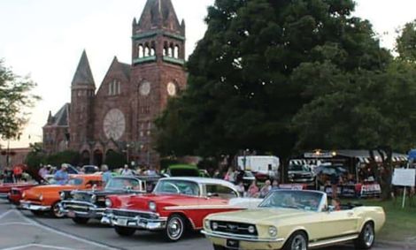 Classic cars lined up at a car show in front of a red brick church