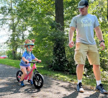 Father walking with a child and the child is riding a bicycle 