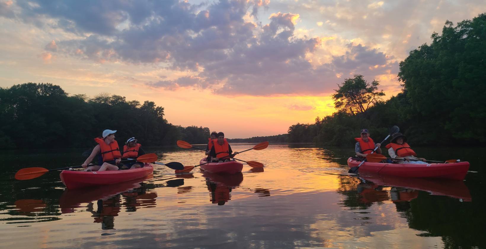 People in kayaks paddling on a river with a sunset in the background