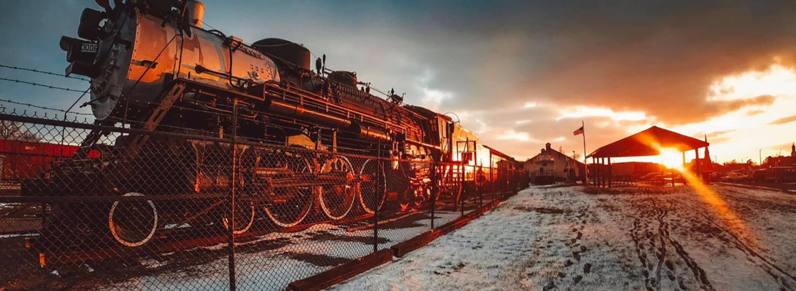 A train in a railroad yard with a beautiful view of the sun in the background